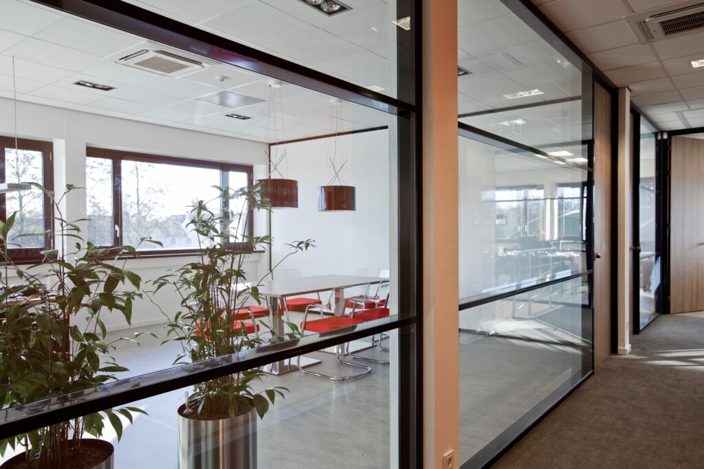 Glazen scheidingswand in een kantooromgeving met tafel en lampen. 