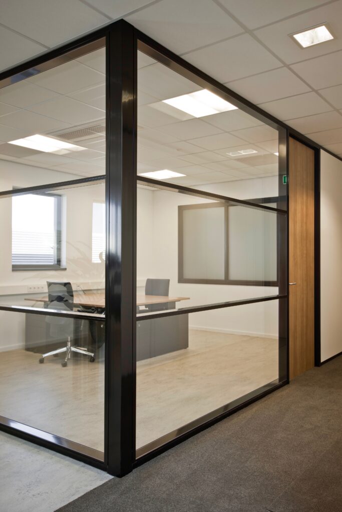 Glazen scheidingswand in een kantooromgeving met bureau en stoelen.