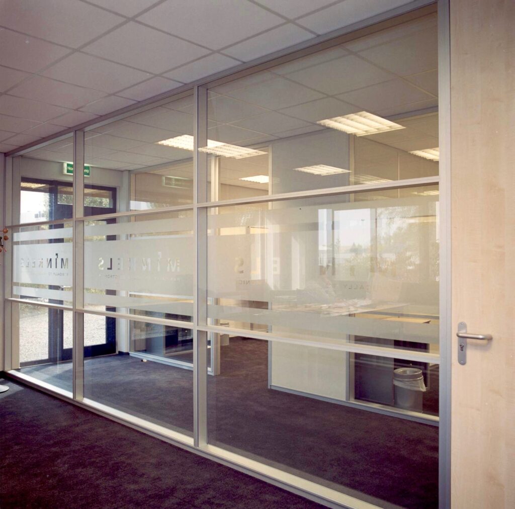 Glazen scheidingswand met belettering in een kantooromgeving.