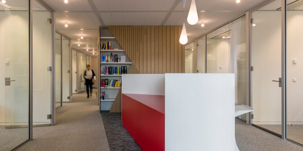 Moderne kantoorreceptie met rode accenten en glazen wanden.