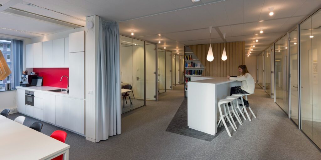 Vrouw werkt aan een bar in een moderne, open kantoorruimte met glazen wanden.