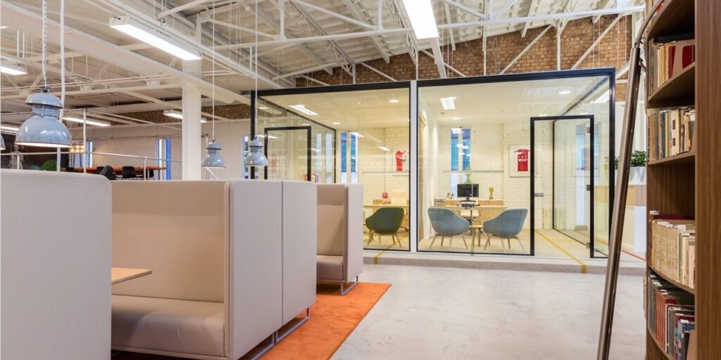 Modern kantoor met werkplekken, glazen vergaderruimte en boekenkast.