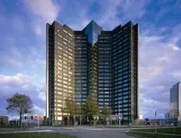 Hoogbouw kantoorgebouw tegen een blauwe lucht met wolken.