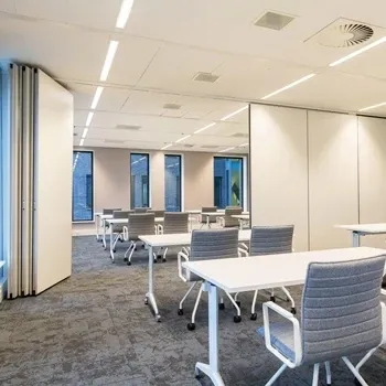 Leeg klaslokaal met witte tafels en grijze stoelen.