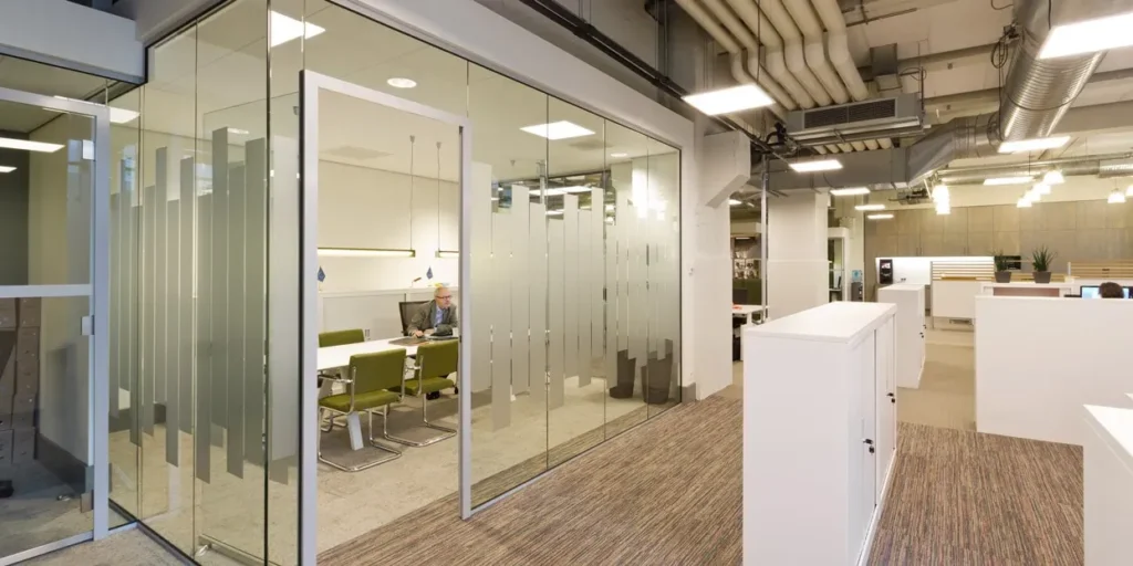 Glazen vergaderruimte in een modern kantoor, met een persoon aan de tafel.