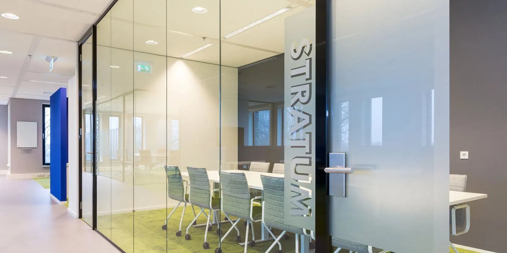 Vergaderruimte met glazen wand en de tekst 'Stratum' in een modern kantoor.