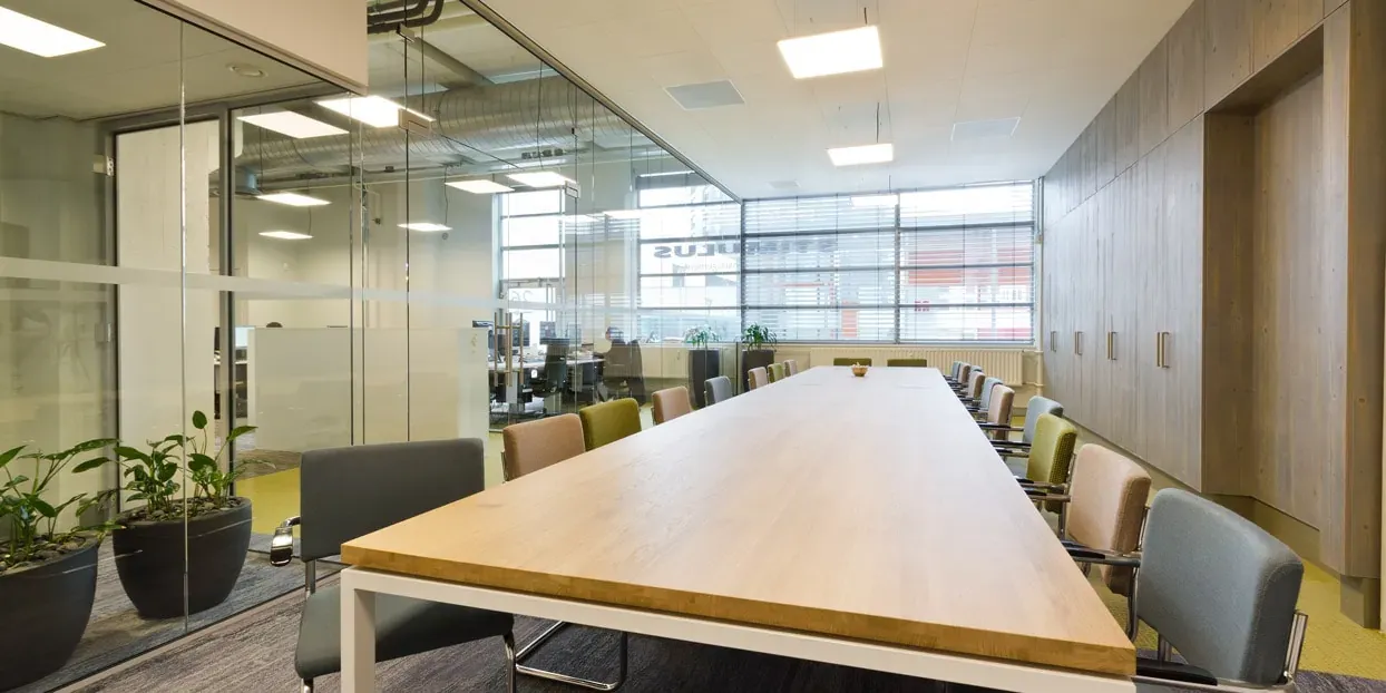 Vergaderzaal met lange houten tafel en stoelen in een modern kantoor.