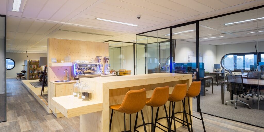 Koffiemachine in kantooromgeving bij een bar met barkrukken.