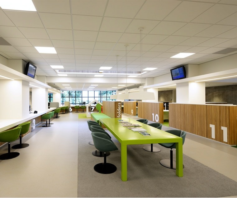 Interieur van een bibliotheek met groene leestafel en stoelen.