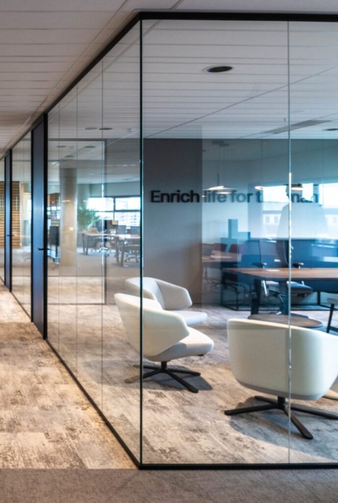 Moderne glazen scheidingswanden in een kantoor met witte fauteuils en een houten vergadertafel.