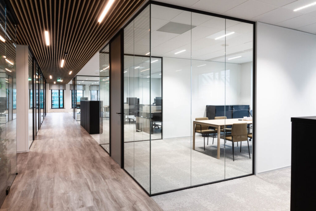 Moderne vergaderruimte met glazen wanden, een houten plafond en een lichte vergadertafel in een kantoorpand.